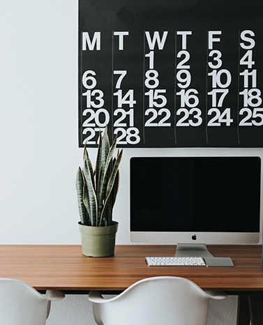 Desktop computer and plant on a desk with calendar on wall