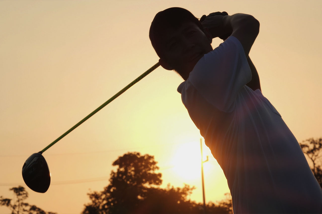 A man swinging a golf club at sunset