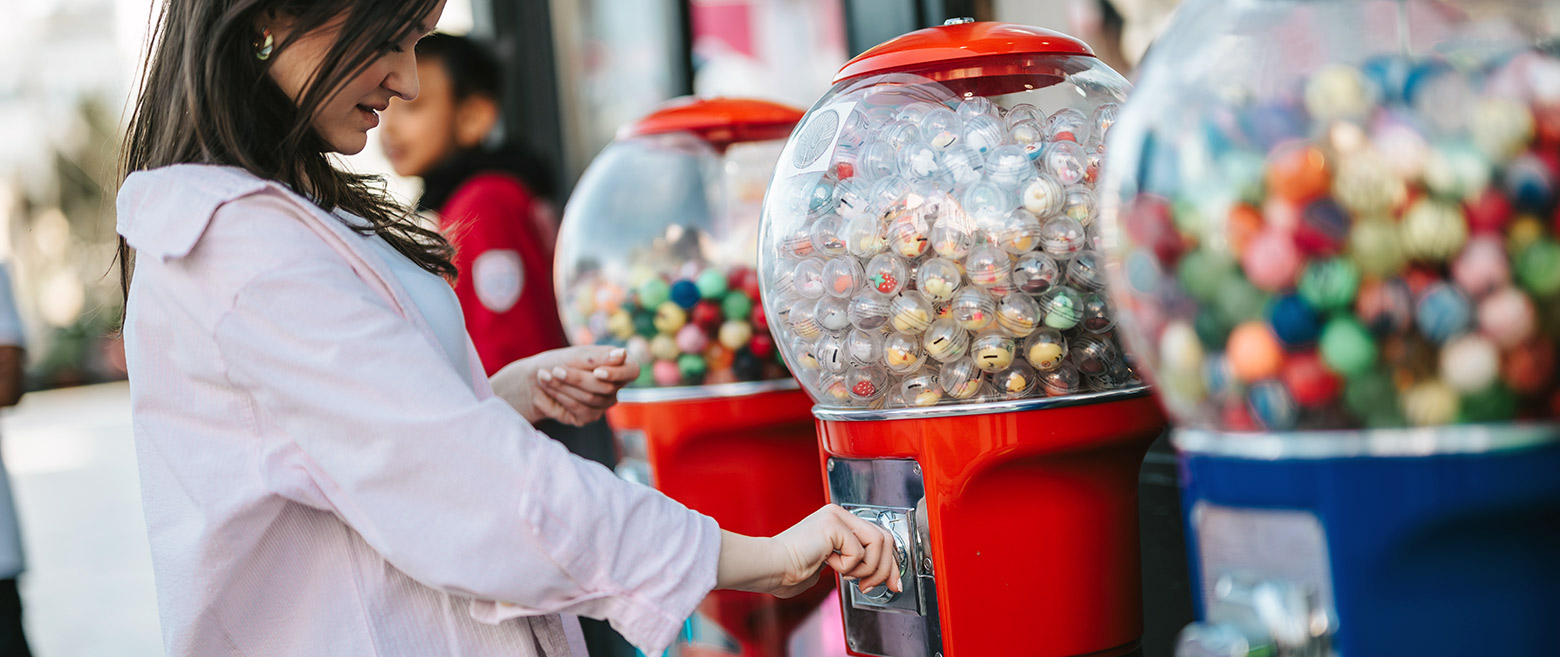 Woman withdrawing prize from a gumball machine. 