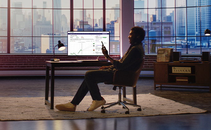 Business professional reviewing financial analytics and growth chart on a desktop monitor at a modern office desk with city skyline windows, planning strategy and budgeting