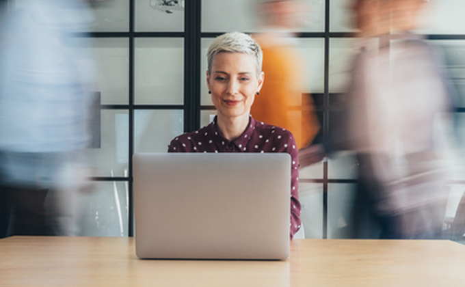 Woman looking down at her computer with people moving behind her