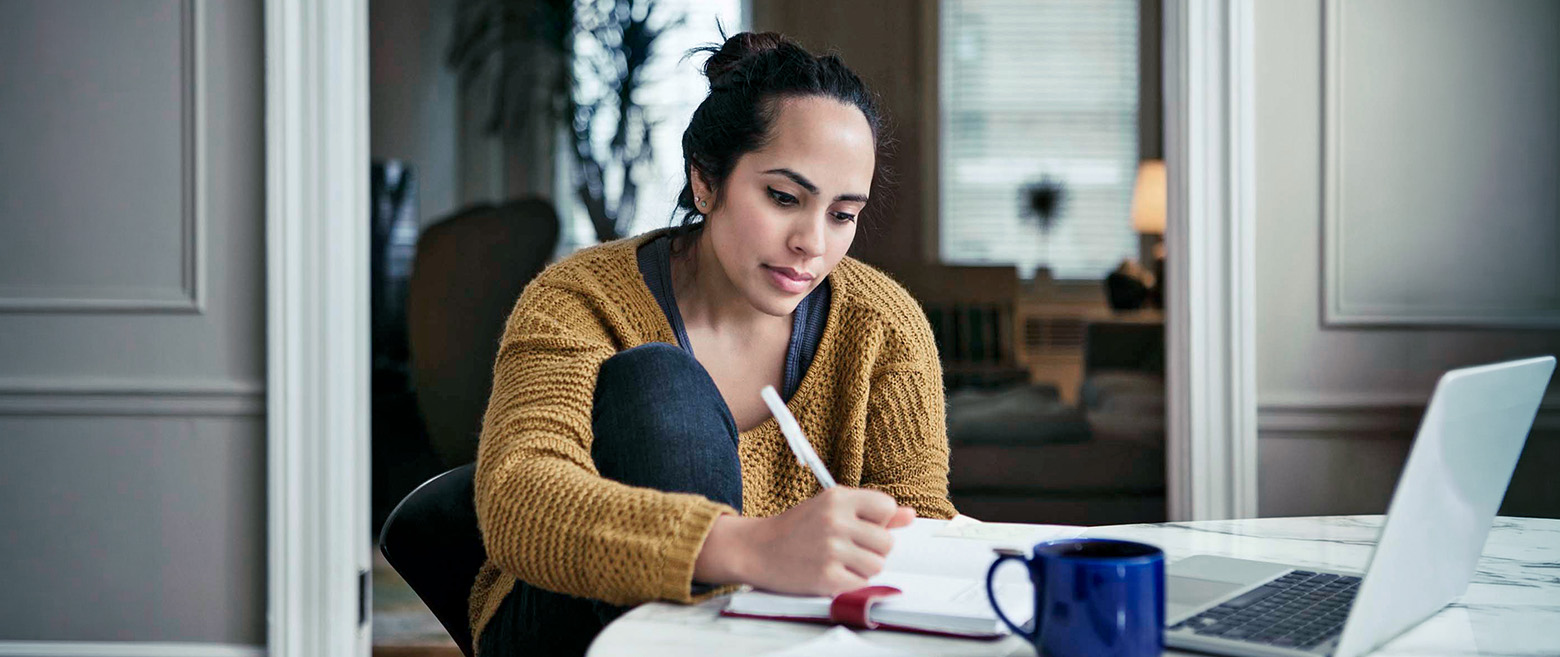 Woman taking notes at a table with a laptop open