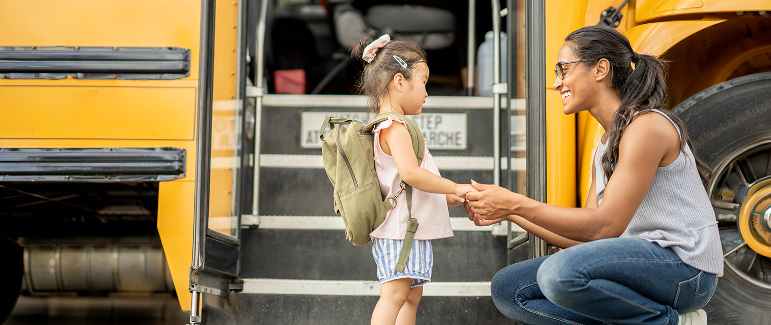 A mother helps her young child board a school bus.