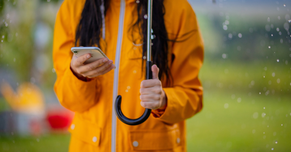 Person in a yellow raincoat holding a phone and umbrella.