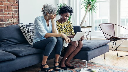 Two people sitting together on a sofa and looking at a tablet in a bright living room