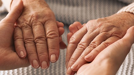 Older adult’s hands resting in a caregiver’s hands