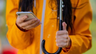 Person in a yellow raincoat holding an umbrella and using a smartphone