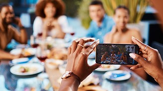 Person using a smartphone to photograph friends gathered around a dining table