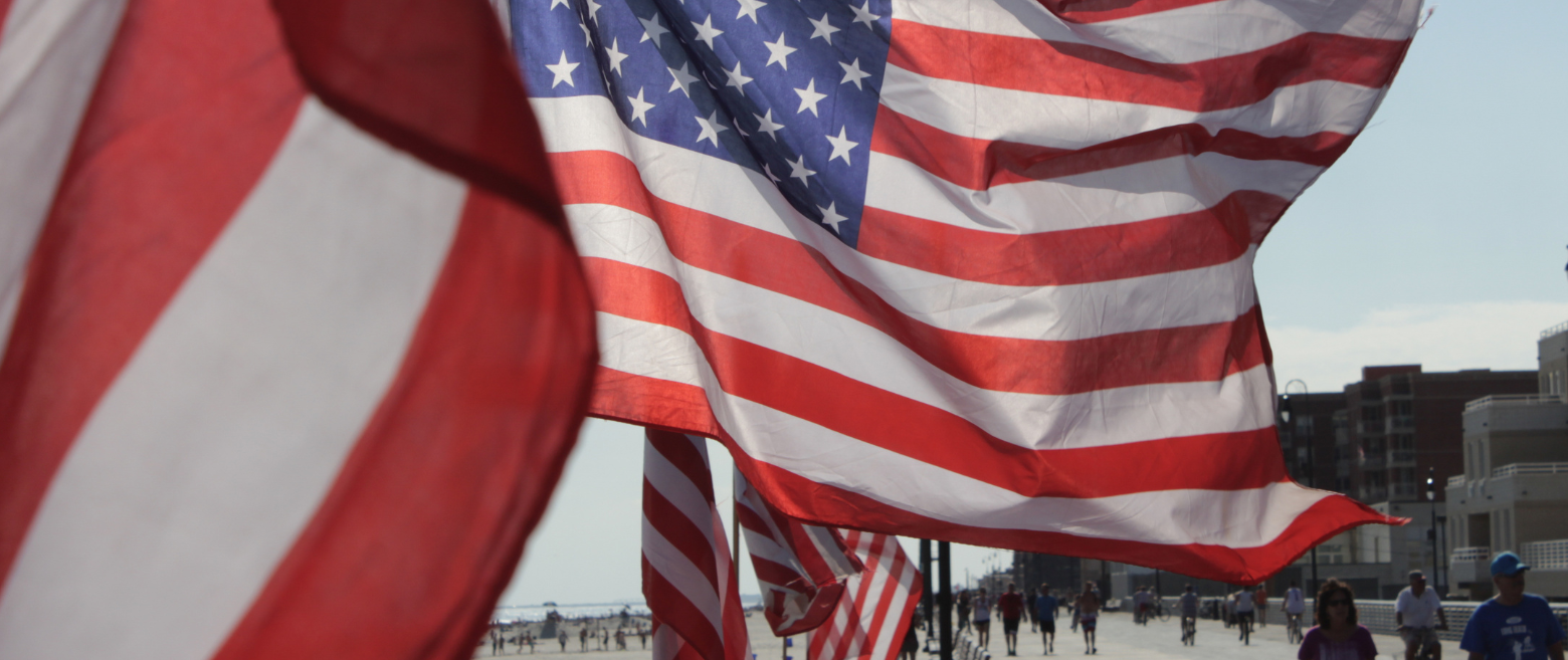 American flags waving along a sunny beach boardwalk.
